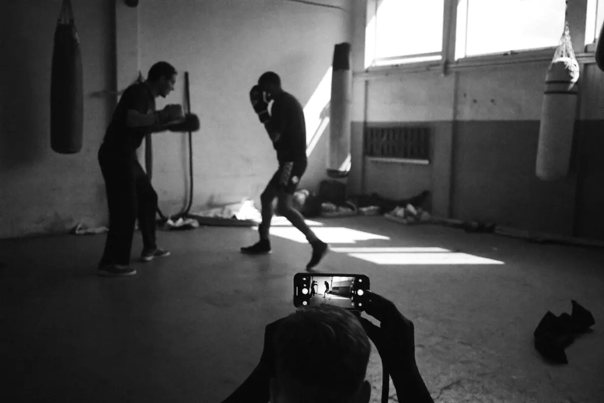 Two boxers on the pads in an old gym, filmed on a phone in the foreground.